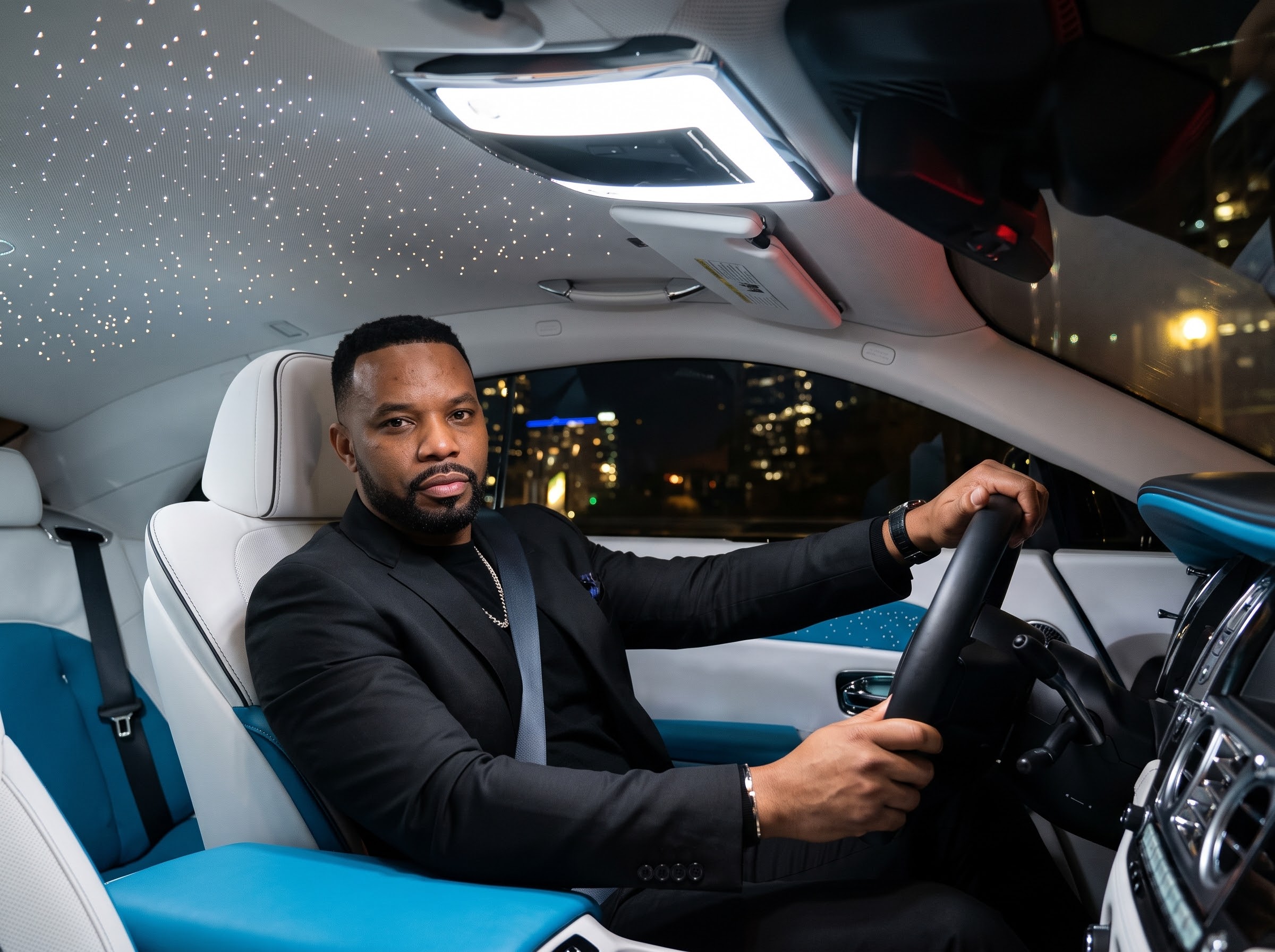David Imonitie at the wheel of a luxury car beneath a starlit ceiling